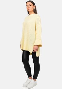 Maglione lavorato a maglia giallo chiaro con maniche ampie, abbinato a leggings in finta pelle neri e sneakers bianche. Motivo testurizzato sul maglione.