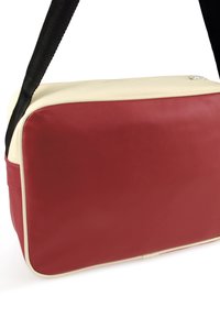 Rote und cremefarbene Schultertasche aus synthetischem Material mit glatter Textur, rechteckiger Form und einem verstellbaren schwarzen Schultergurt. Reißverschluss oben.