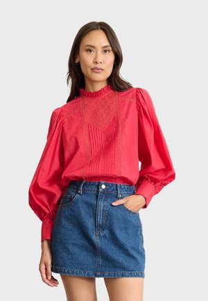 Blouse en coton rouge avec col à volants, manches ballons et broderies détaillées à l'avant, associé à une mini jupe en denim.