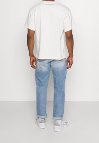 Vit bomullströja med korta ärmar, med text på ryggen. Ljusblå denimjeans med uppvikta ben. Grå och vita sneakers.