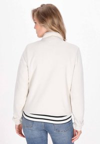 Giacca in pile bianca con colletto alto, caratterizzata da un orlo a strisce bianche e nere, dalla texture morbida e da una vestibilità casual e rilassata.