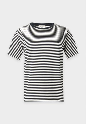 Personne portant un t-shirt rayé noir et blanc, une longue jupe en dentelle crème, des bottes noires et tenant un petit sac à main bleu avec une bandoulière chaîne.