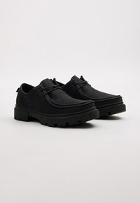 Zapatos negros con un upper liso, detalles de costura, diseño con cordones y suelas de goma gruesas y resistentes. Estilo minimalista con características prácticas.