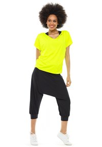 Lime green loose-fitting T-shirt with short sleeves paired with black, draped harem pants featuring elastic cuffs and a smooth texture.