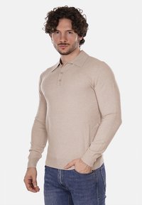 Polo a maniche lunghe beige con colletto classico e patta con tre bottoni, realizzato in tessuto morbido. Presenta maniche aderenti e una texture liscia.