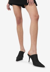 Mule nere con tacco alto e punta appuntita, caratterizzate da una tomaia texturizzata e un design aperto sul retro, che offre una calzata aderente intorno al piede.