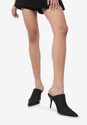 Mule nere con tacco alto e punta appuntita, caratterizzate da una tomaia texturizzata e un design aperto sul retro, che offre una calzata aderente intorno al piede.