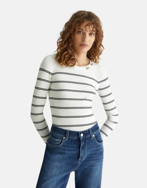 Top bianco a maniche lunghe con righe orizzontali nere e scollatura rotonda, abbinato a jeans blu a vita alta.