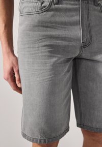 Gray denim shorts with a straight cut, featuring visible stitching, pockets, and a distressed texture. Hemmed at the knees.