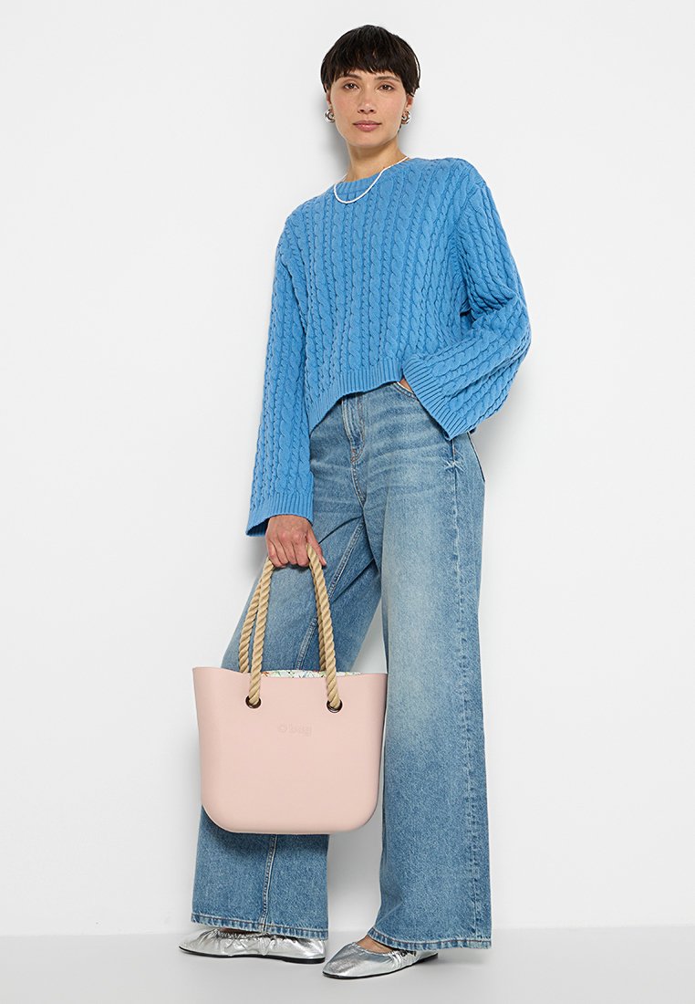 Niebieski sweter w sploty, szerokie wyblakłe dżinsy i różowa torba na ramię z plecionymi uchwytami. Srebrne buty dopełniają stylizację, a całość uzupełnia prosta naszyjnik.