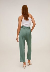 Pantalon vert clair taille haute, coupe décontractée avec poches latérales, associé à un débardeur blanc en côtes, porté avec des talons de couleur claire.