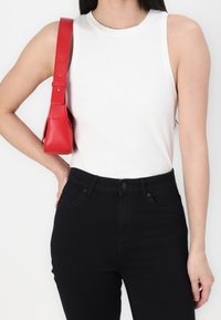 Vit ribbad tanktop kombinerad med högmidjade svarta jeans. En liten röd handväska ger en färgklick med en strukturerad design och justerbart band.