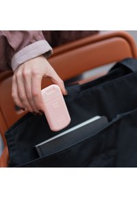 Botella rosa etiquetada como "Rosa Brillante" siendo levantada de una bolsa tote negra, con un cuaderno gris parcialmente visible dentro de la bolsa.