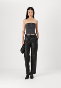 Pantaloni neri in ecopelle abbinati a un top bustier in denim grigio, con zip frontale e silhouette aderente. Il modello tiene una borsa nera.