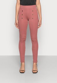 Rosa åtsittande byxor i stretchigt tyg med hög midja och dekorativa guldknappar framtill. Stylat med svarta klackar.