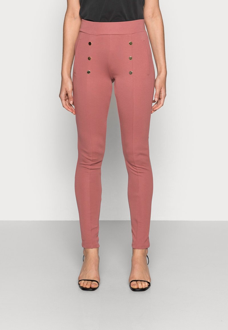 Rosa åtsittande byxor i stretchigt tyg med hög midja och dekorativa guldknappar framtill. Stylat med svarta klackar.