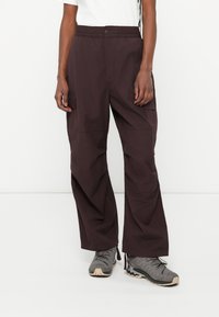 Pantaloni cargo in tessuto viola scuro con vita elastica e numerose tasche laterali. Vestibilità ampia con una leggera texture.