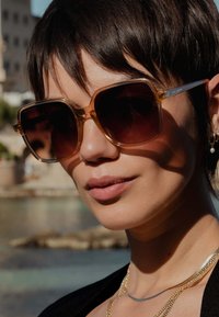 Lunettes de soleil oversize dégradées brunes avec des montures transparentes couleur miel. Présentent un design géométrique et des accents en métal sur les côtés.