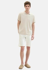 Beige, short-sleeve polo shirt with a collar, paired with white shorts. Worn with light brown slip-on shoes. Simple, casual design.
