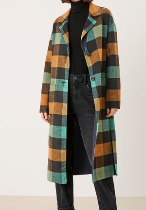 Manteau long à carreaux avec des motifs verts, marron et noirs. Confectionné dans un tissu épais et texturé, doté d'un col cranté et de boutons sur le devant.
