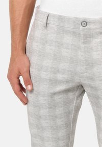 Pantaloni gri deschis cu un model texturat în carouri. Dispune de o închidere cu buton și buzunare laterale, cu un finisaj de țesătură netedă.