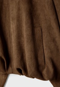 Giacca in camoscio marrone caratterizzata da una texture morbida, orlo elastico e tasca nascosta, con una finitura liscia e un design elegante.