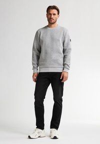 Grijze sweater met een textuurpatroon, ronde hals en boordjes, gecombineerd met zwarte jeans en witte sportschoenen.