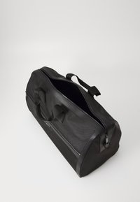 Sac de sport noir avec une surface texturée, poignées doubles, ouverture zippée et matériau synthétique. Doté d'accents contrastants ressemblant à du cuir.