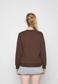 Brun sweatshirt med rund halsringning och ribbade muddar, kombinerad med en ljus denim plisserad kjol, som visar en avslappnad lager-på-lager-design.