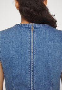 Vestido de denim con cuello redondo, diseño sin mangas y un cierre de cremallera de metal visible en la parte posterior, con una tela azul texturizada.