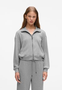 Grau zip-up Sweatshirt mit hohem Kragen, gerippten Bündchen und elastischem Saum. Das Material scheint weich und strukturiert zu sein und weist ein Logo-Detail auf.