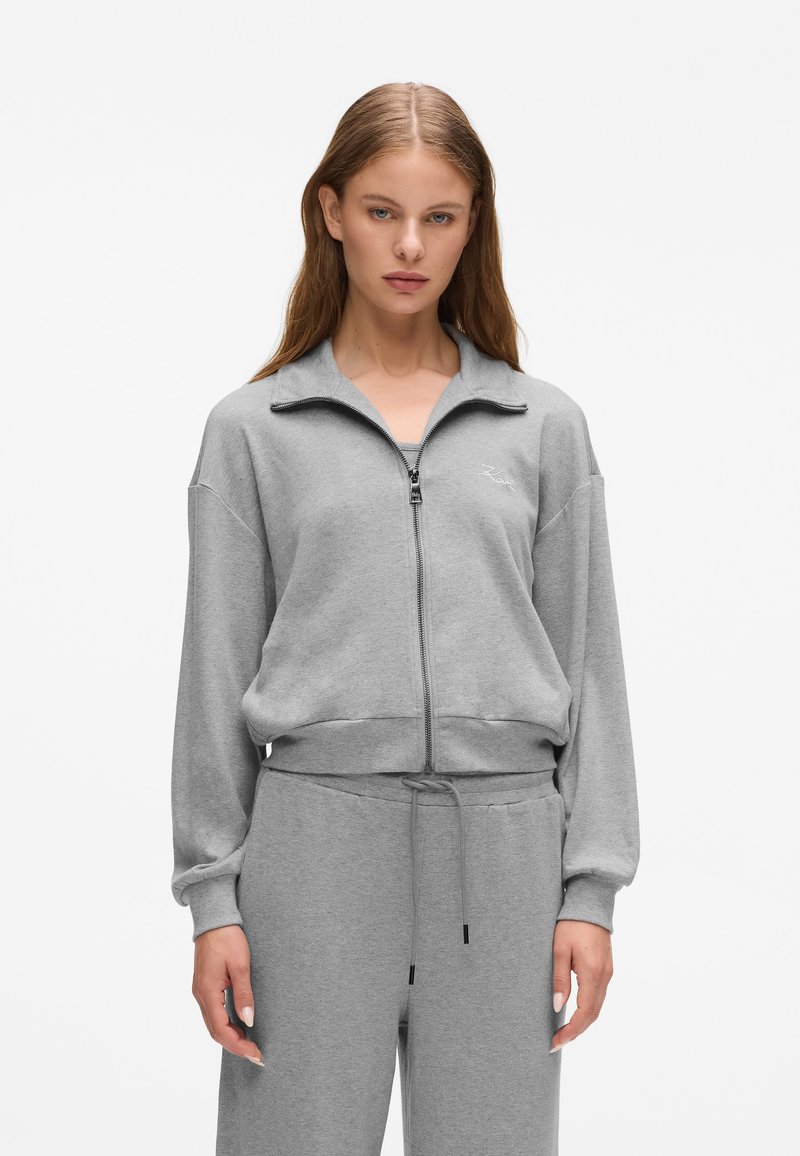 Grau zip-up Sweatshirt mit hohem Kragen, gerippten Bündchen und elastischem Saum. Das Material scheint weich und strukturiert zu sein und weist ein Logo-Detail auf.