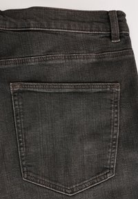 Détail de la poche arrière d’un jean en denim noir délavé avec couture visible et passant de ceinture sur fond blanc.