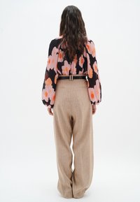 Blommig blus med svart bas och orange/rosa mönster, ihop med beiga högmidjade, randiga vida byxor. Svart bälte som accent.