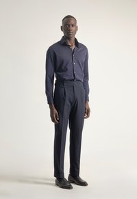 Camisa de manga larga azul marino con botones, combinada con pantalones azul marino a medida con cintura alta y dos botones decorativos. Calzado negro.