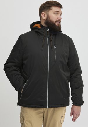 Schwarze isolierte Jacke mit Kapuze, ausgestattet mit einem Frontreißverschluss, einer Brusttasche und Zugbandakzenten. Das Innenfutter ist orange.