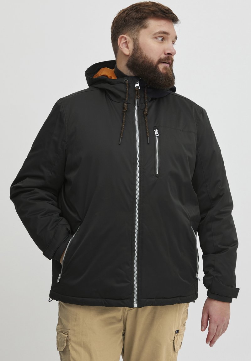 Svart isolerad jacka med huva, som har en framzipper, bröstficka och dragskoaccenter. Insidan är orange.