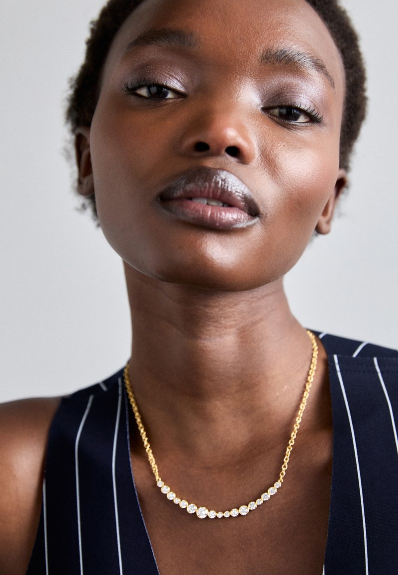 Χρυσή αλυσίδα λαιμού με στρογγυλά ασημένια στοιχεία σε γραμμικό σχέδιο. Το μοντέλο φοράει ένα ναυτικό ρούχο με λευκές ρίγες.