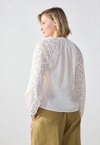 White blouse with embroidered, eyelet-patterned sleeves and a gathered neckline, paired with khaki wide-leg pants.