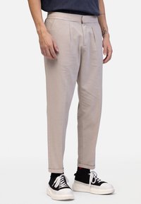 Jasnobeżowe chinosy zwężane ku dołowi z zakładkami z przodu, płaskim pasem i kieszeniami po bokach. W połączeniu z czarno-białymi trampkami.