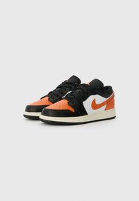 Sneakers basse in pelle nera, arancione e bianca. Presentano una punta perforata, uno swoosh bianco e una suola in gomma testurizzata. Lacci e dettagli neri.