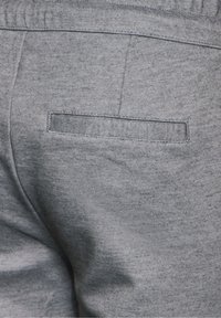 Grå tygbyxor med en strukturerad design, elastisk midja och en bakficka med enkel sömdetalj.