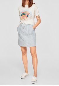 Světle šedé tričko s designem barevných bambulek a krátkými rukávy. Sukně s modro-bílými pruhy a stahovacími šňůrkami v pase, s bočními kapsami. Bílé tenisky.