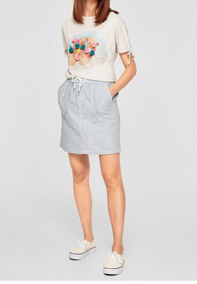 Světle šedé tričko s designem barevných bambulek a krátkými rukávy. Sukně s modro-bílými pruhy a stahovacími šňůrkami v pase, s bočními kapsami. Bílé tenisky.