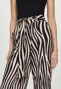 Pantalon à jambes larges de couleur crème avec des rayures zèbre noires, doté d'une taille nouée. Le tissu présente une texture douce et un design fluide.