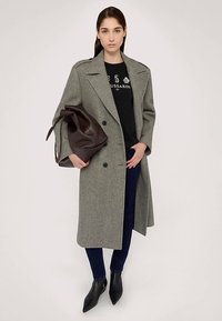 Šedý vlněný trenčkot s nadměrným střihem, dvouřadé knoflíky, černé tričko, tmavé džíny a hnědá kožená taška přes rameno.