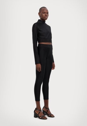 Top corto nero con scollatura alta e vita elastica, abbinato a leggings neri con una vita simile. Indossato con sandali neri con tacco.