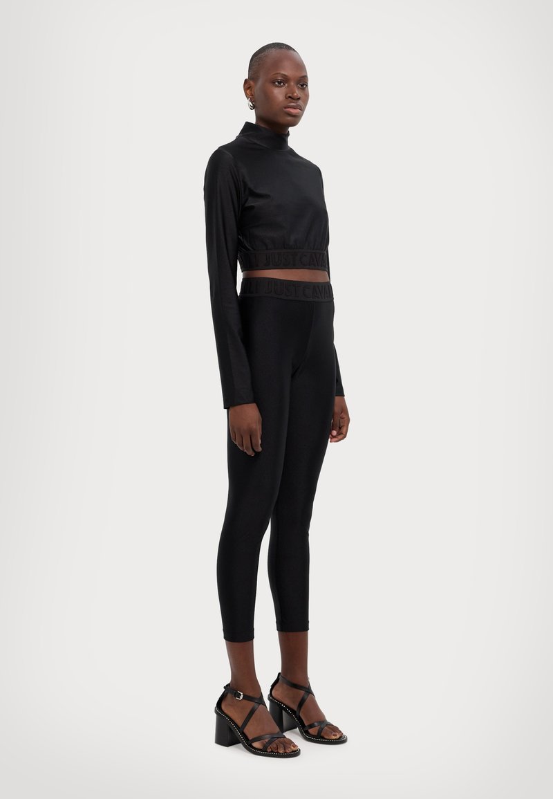 Black crop top with a high neckline and elastic waistband, paired with black leggings featuring a similar waistband. Worn with black heeled sandals.
