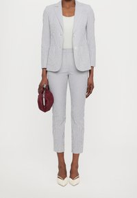 Pruhovaný blazer a odpovídající zkrácené kalhoty v světle modré a bílé, v kombinaci s bílým topem a bordó psaníčkem. Elegantní špičaté podpatky.