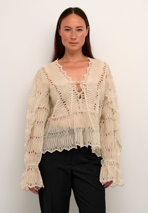 Beige kanten top met uitsnijdingen, een V-hals en trompetmouwen. Heeft een strikdetail aan de voorkant, wat een gelaagde uitstraling creëert.